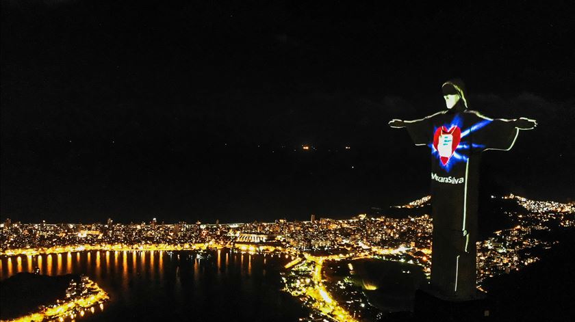 A estátua do Cristo Redentor do Rio de Janeiro mostrou-se no domingo com máscara de proteção para alertar a população para o seu uso durante a pandemia da Covid-19. Foto: António Lacerda/EPA